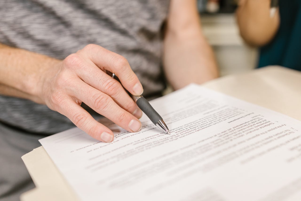 heros-img Close-up of a person's hand signing an important legal document with a pen indoors.
